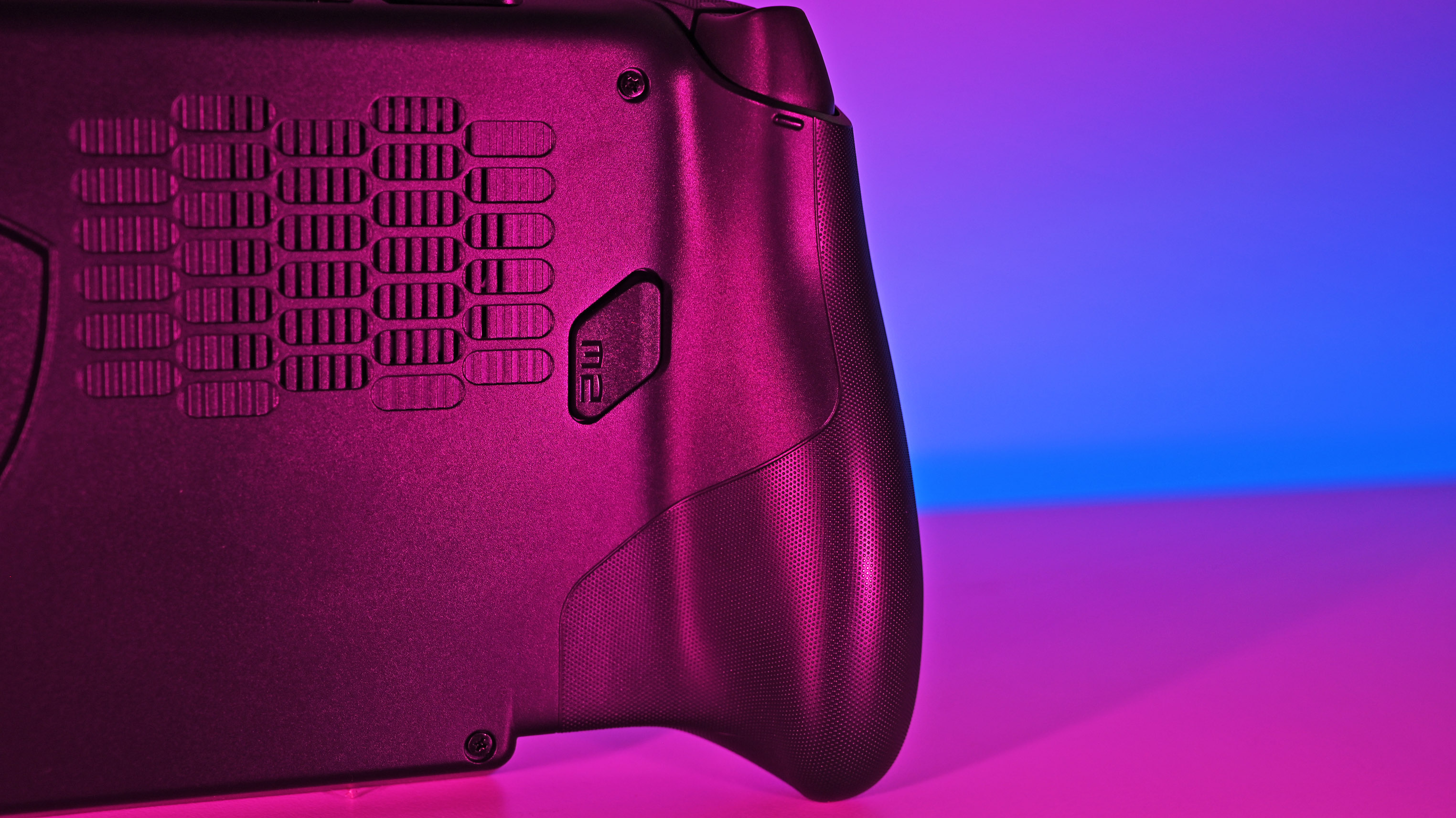 Close-up of the back right side of the device under pink studio light, showing the rear cooling intake grille, textured grip, and a remappable macro button labeled M2.