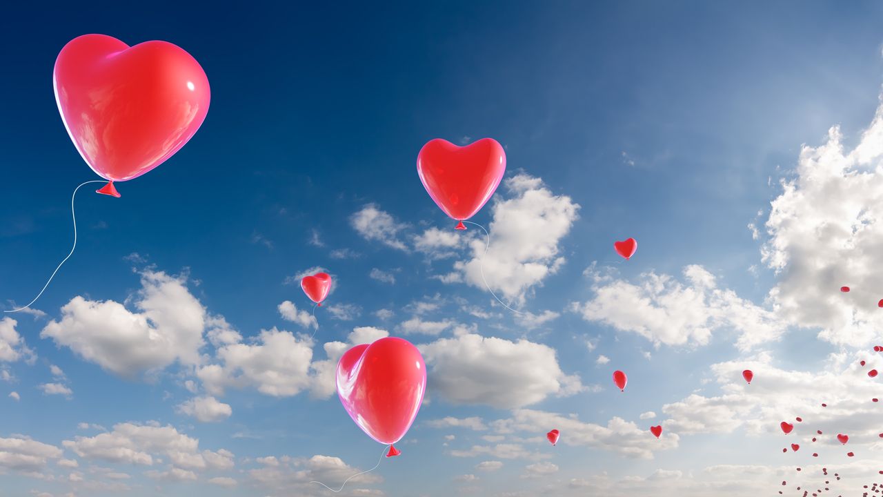 Red balloons shaped like hearts float into a pretty blue sky.