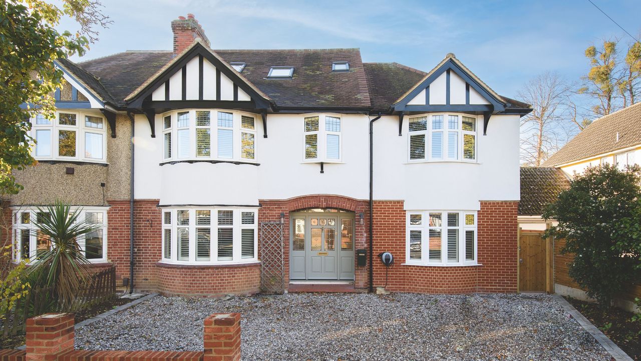 Exterior shot of a large semi-detached house with a mixture of white render and red brick, with a gravel driveway in front