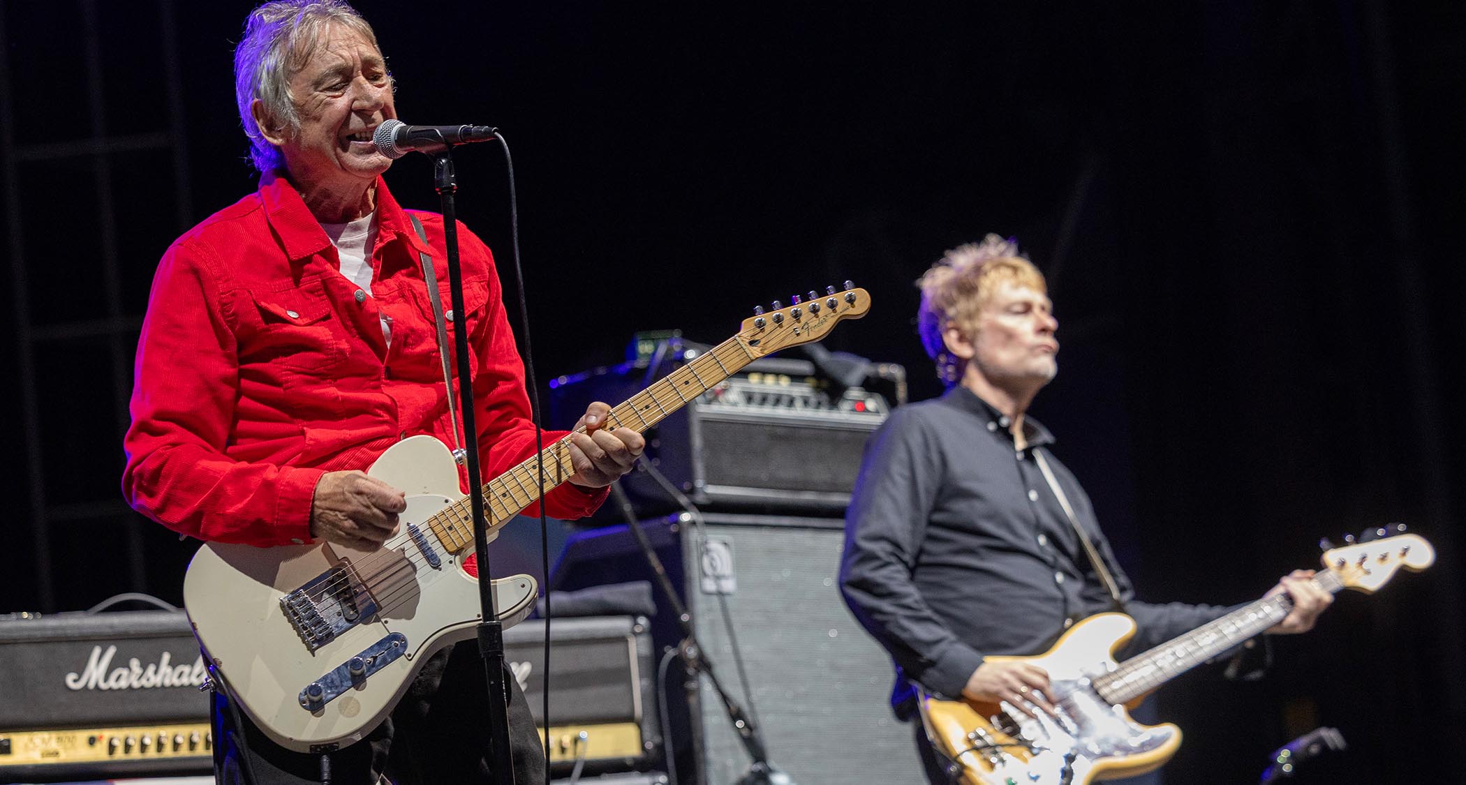 Steve Diggle wears a red shirt and plays a Telecaster onstage with the Buzzcocks
