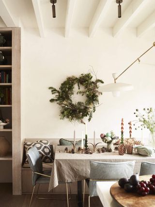 Green, natural Christmas wreath hanging over a festive set dining table in a white kitchen