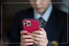 A close up of a boy in school uniform using an iPhone