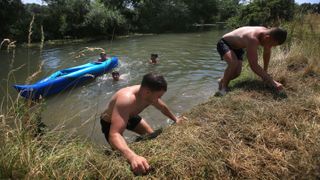 Wild swimmers enjoy the hottest day ever in the UK using tufts of grass to pull themselves out of the river