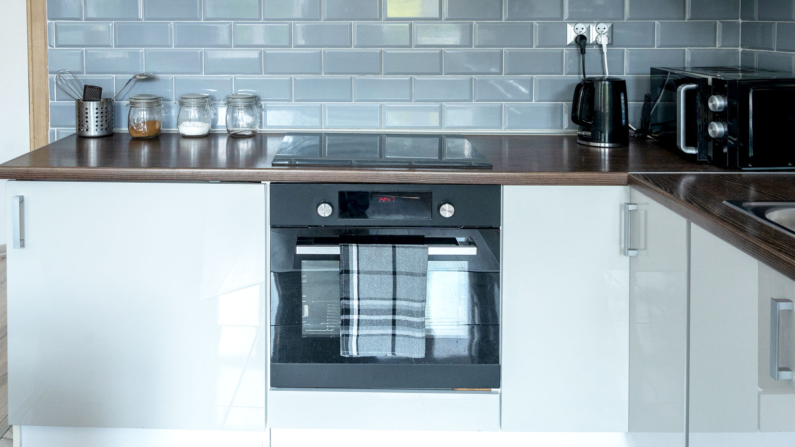 Contemporary white gloss kitchen cabinets and doors with a dark worktop and grey metro tiles