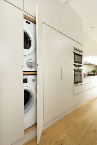 Utility room storage, washing machine and tumble dryer integrated into cream kitchen cabinets beside double oven and handleless drawers