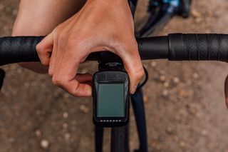 A hand is reaching out to a Garmin bike computer which is mounted on handlebars