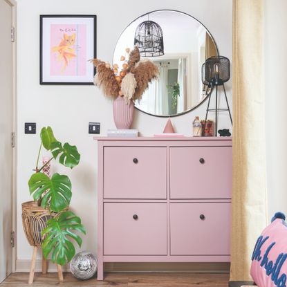 A hallway with a pink shoe cabinet and a round mirror on the wall above it