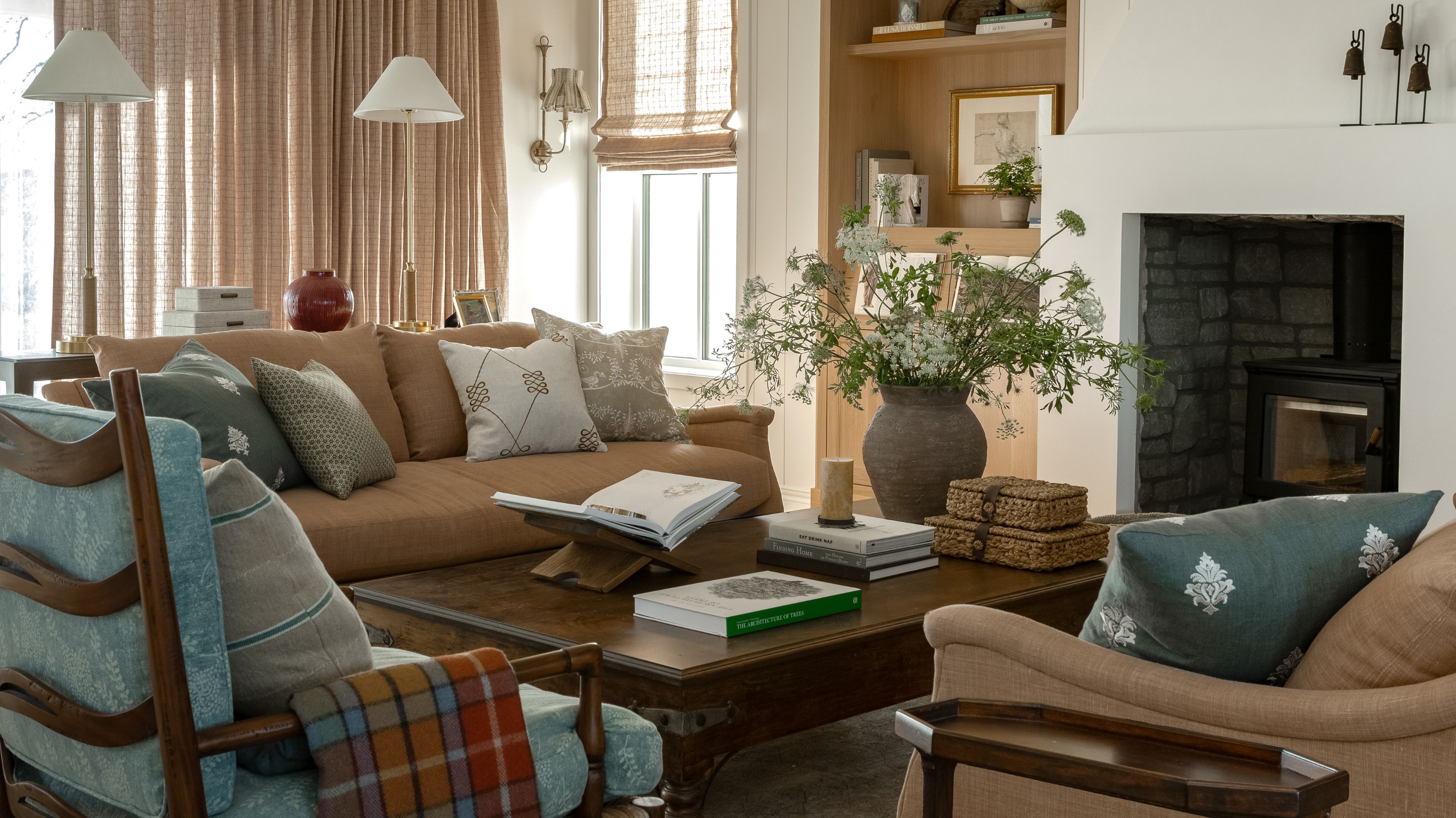 a cozy layered living room with apricot upholstery, oak built-ins, dark wooden coffee tale and blue floral prints on pillows and newly upholstered antique wooden arm chairs