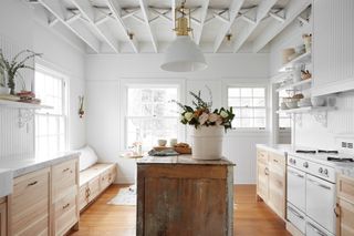 kitchen with pale colorscheme and wooden cabinetry. A reclaimed island stands in center