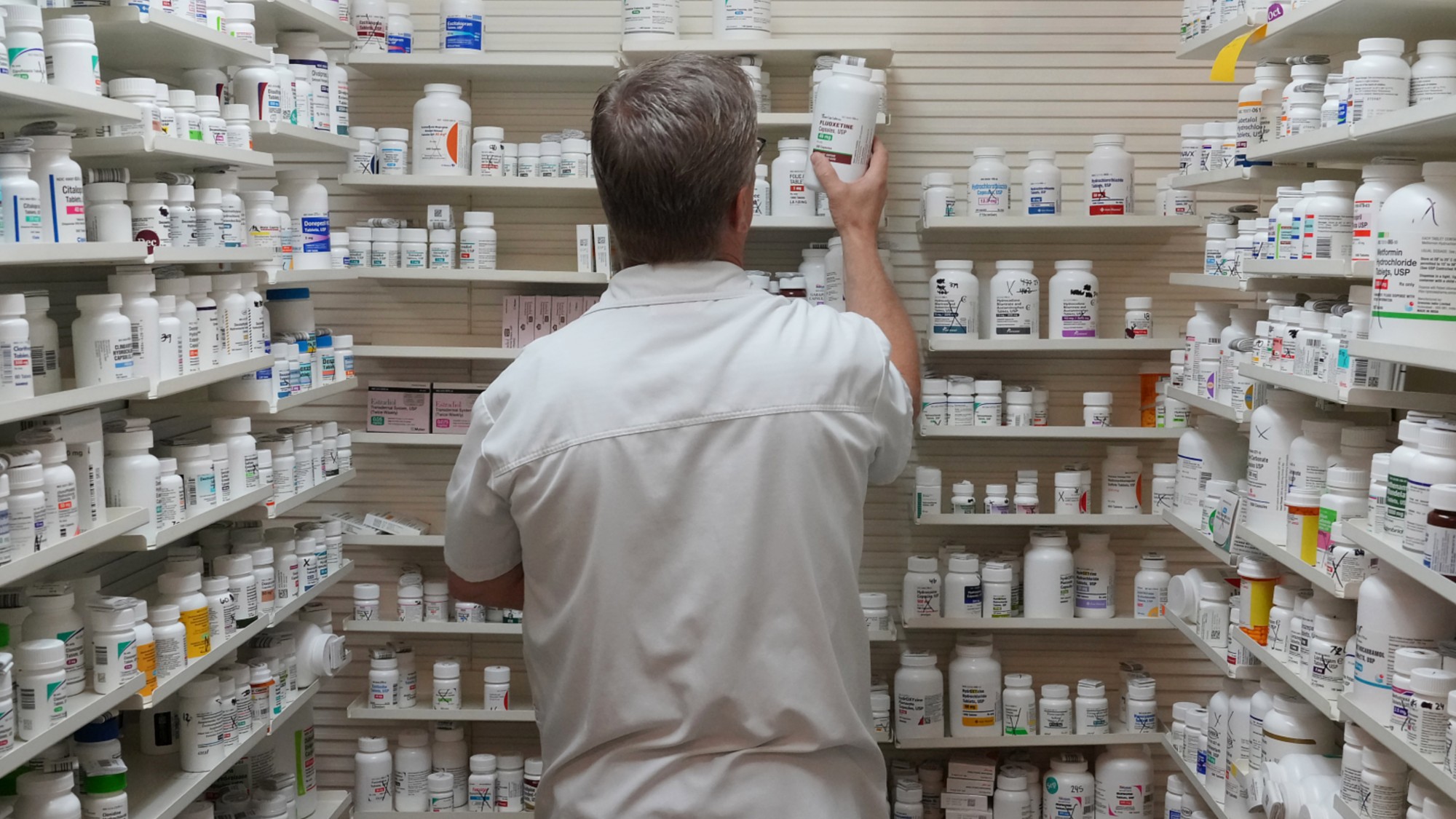 A pharmacist pulls a drug from a shelf inside a pharmacy