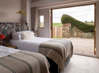 twin bedroom with patterned headboard and huge window open and overlooking stone wall and green fields