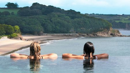 Rear view of two women looking from an infinity pool towards a bay and trees