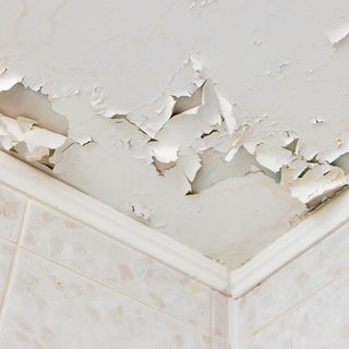 white peeling paint on a ceiling in the corner of a room, with wall tiles