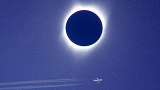 total eclipse with white corona and a airplane flying beneath it. 