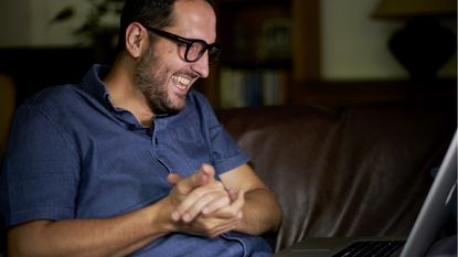 An investor sits with his laptop open on his lap and rubs his hands together in anticipation of checking his portfolio.