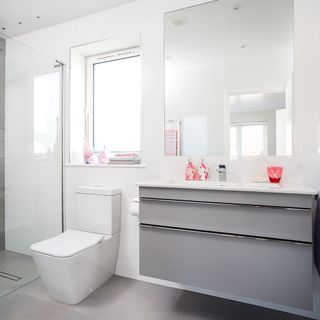 A white bathroom with toilet, walk in shower and wall hung sink vanity unit with pink accessories