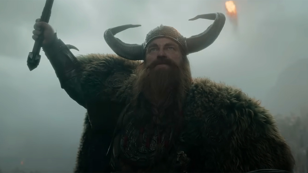 Gerard Butler in full Viking gear and raising a weapon toward the sky as a fireball lights the sky behind him.