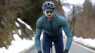 Cyclist climbing on the road with snow down the sides wearing rh+ kit