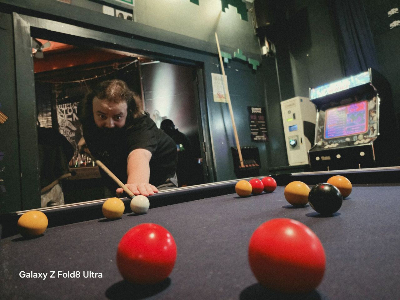 Man leaning over a pool table to take a shot in a dimly lit bar, with colorful balls scattered across the table.