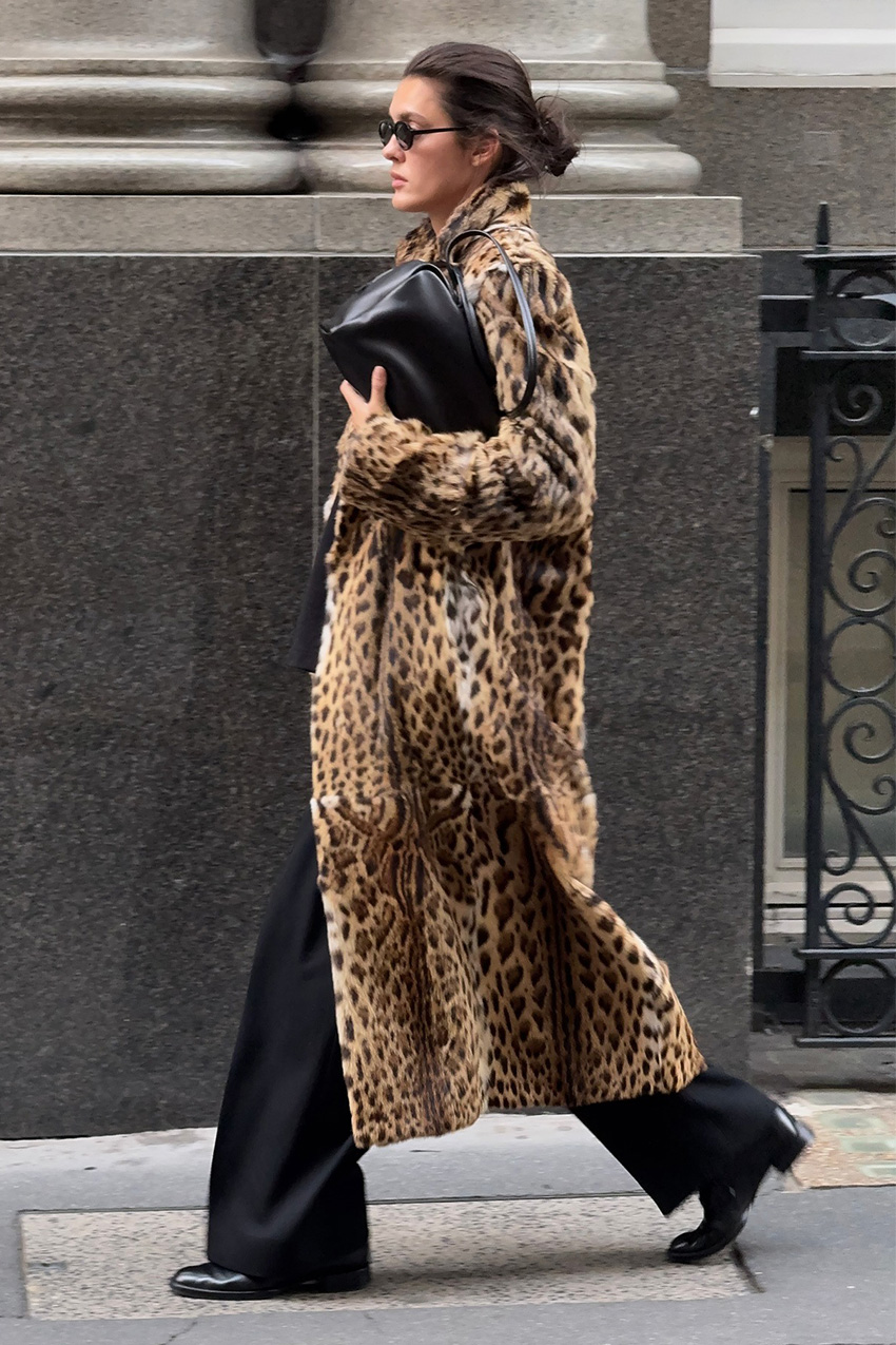 Trendy basics at Nordstrom are shown in a street style photo of a woman walking down the sidewalk wearing black oval sunglasses styled with a long leopard print fur coat layered over black trousers worn with a black bowler black and black ankle boots