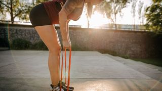 Woman standing on resistance band, holding ends in hands and bending over at hips