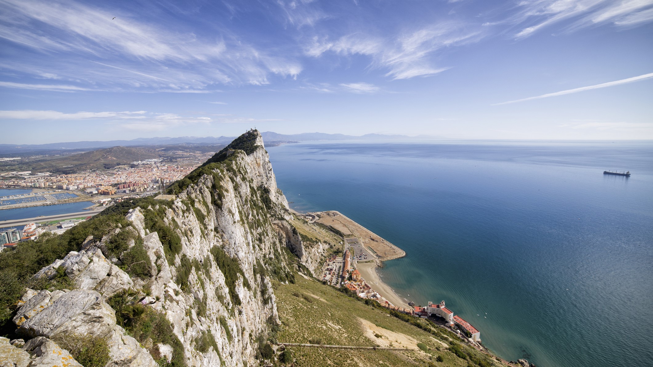 aerial view of Gibraltar rock in the foreground and a vast body of water in the background with a partly cloudy sky above.