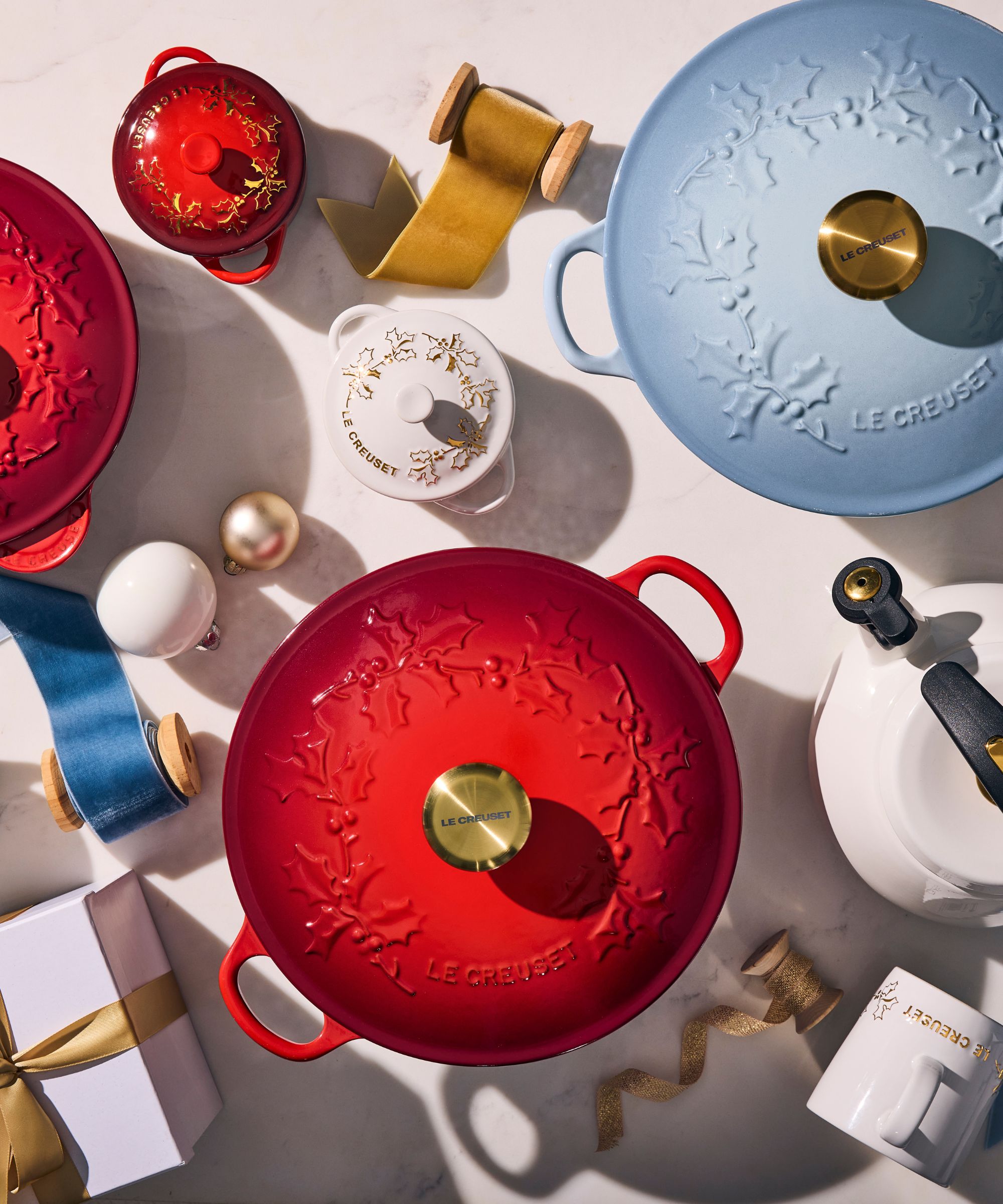 Sky blue, white and red Le Creuset pots with holly decor on the lids