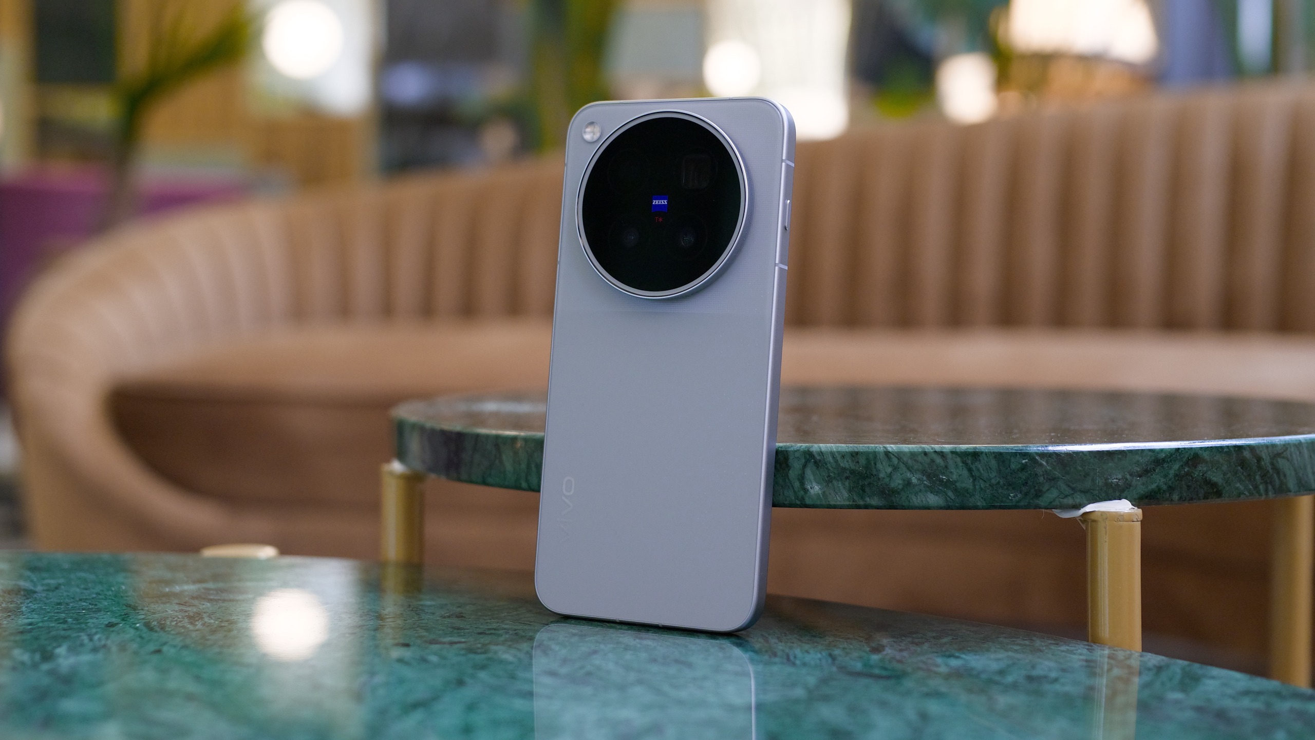 Vivo X500 Pro Max standing upright on a green marble table in a softly lit interior, with its large circular rear camera module facing the camera.