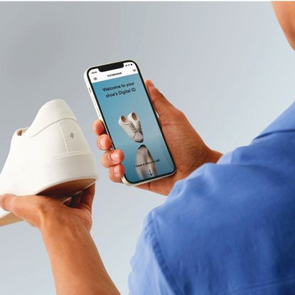 A man using a smartphone to scan a digital ID tag on the back of a white sneaker