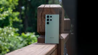 The green Samsung Galaxy S23 Ultra leaning against a wooden deck railing