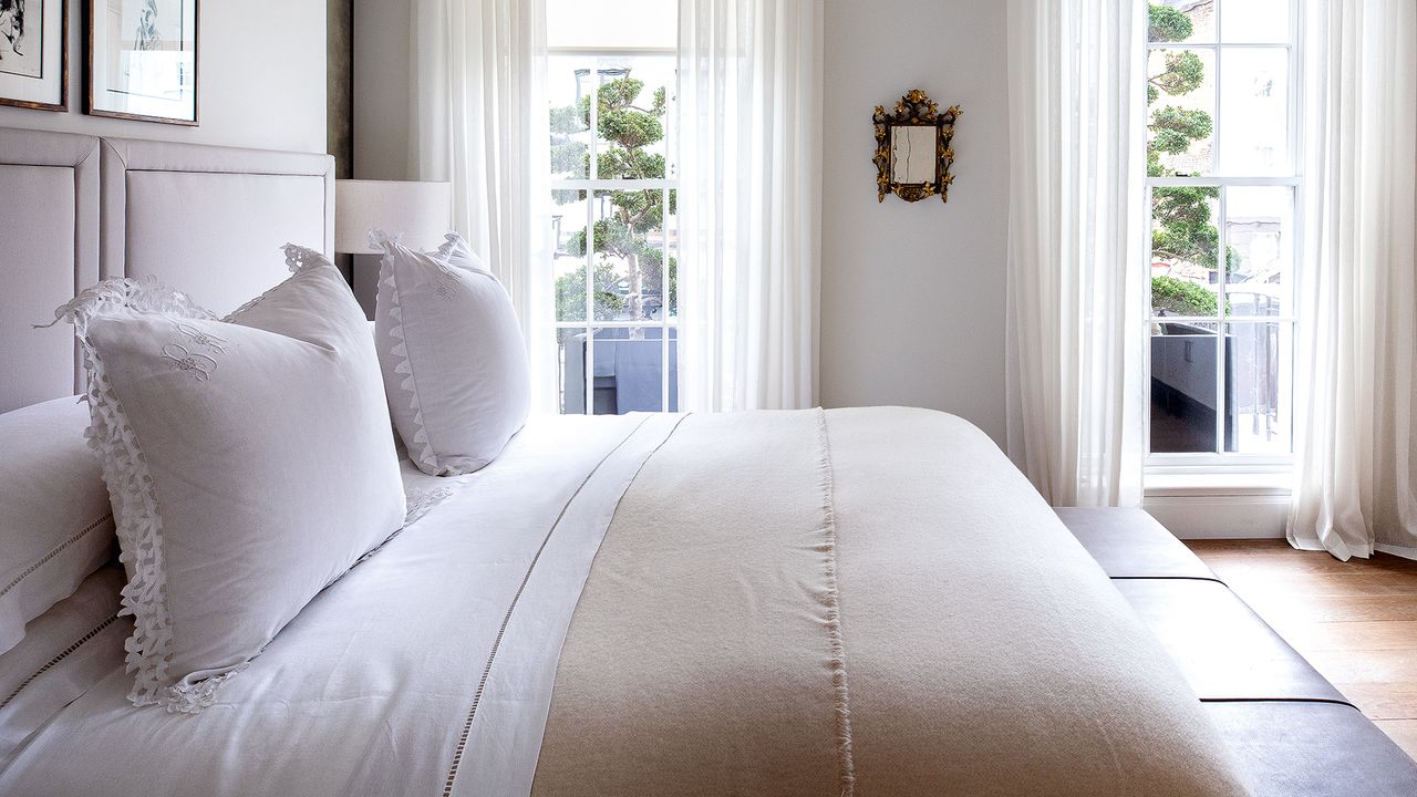 A bedroom with white bedding and two floor length windows