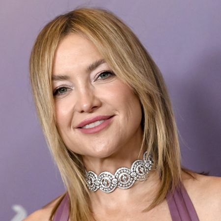 a white woman with short, blonde hair poses in front of a lavender backdrop