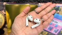 An open palm holding an earbud each of the Apple AirPods 5 with Wireless Charging Case and AirPods 4 with ANC.