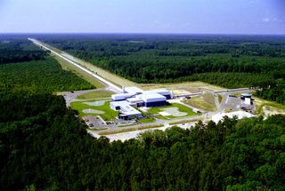 The LIGO project's gravitational-wave detector facility in Livingston, Louisiana, a complex of white buildings surrounded by lush green forest.