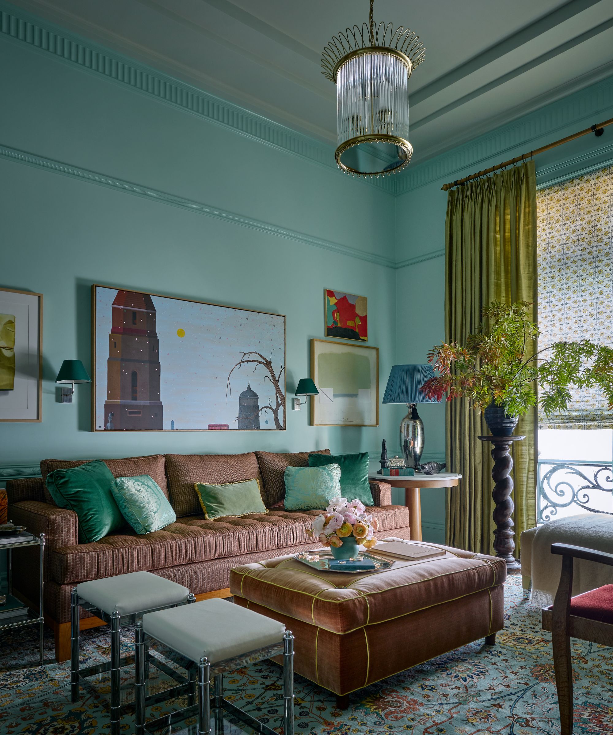 A maximalist living room with blue-green color-drenched walls and trim and a gray-green ceiling. A brass and glass pendant light, moss-green drapes, a brown-pink sofa with emerald-green cushions, and a gallery wall of artwork.