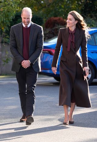 Kate Middleton and Prince William walking in maroon outfits and smiling