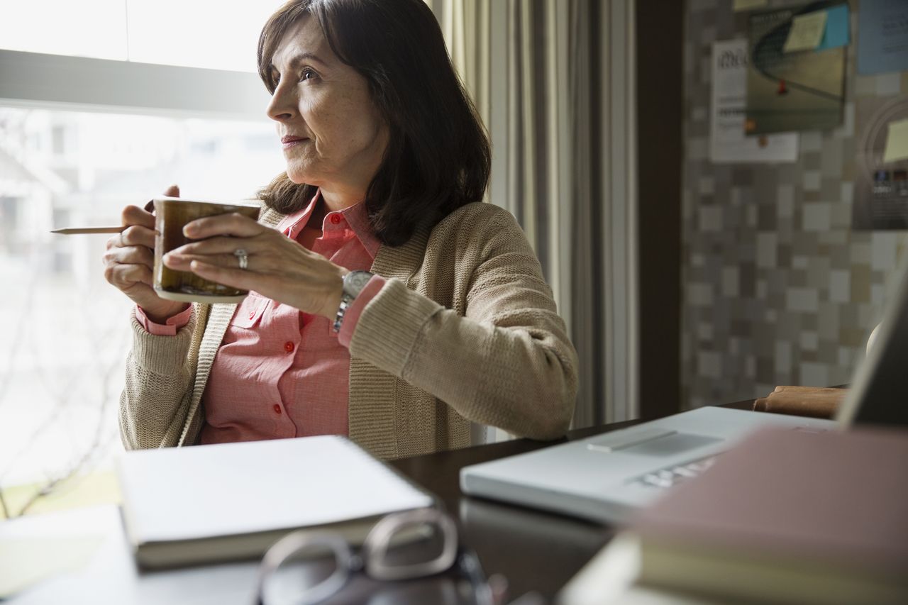 Pensive woman drinking coffee in home office