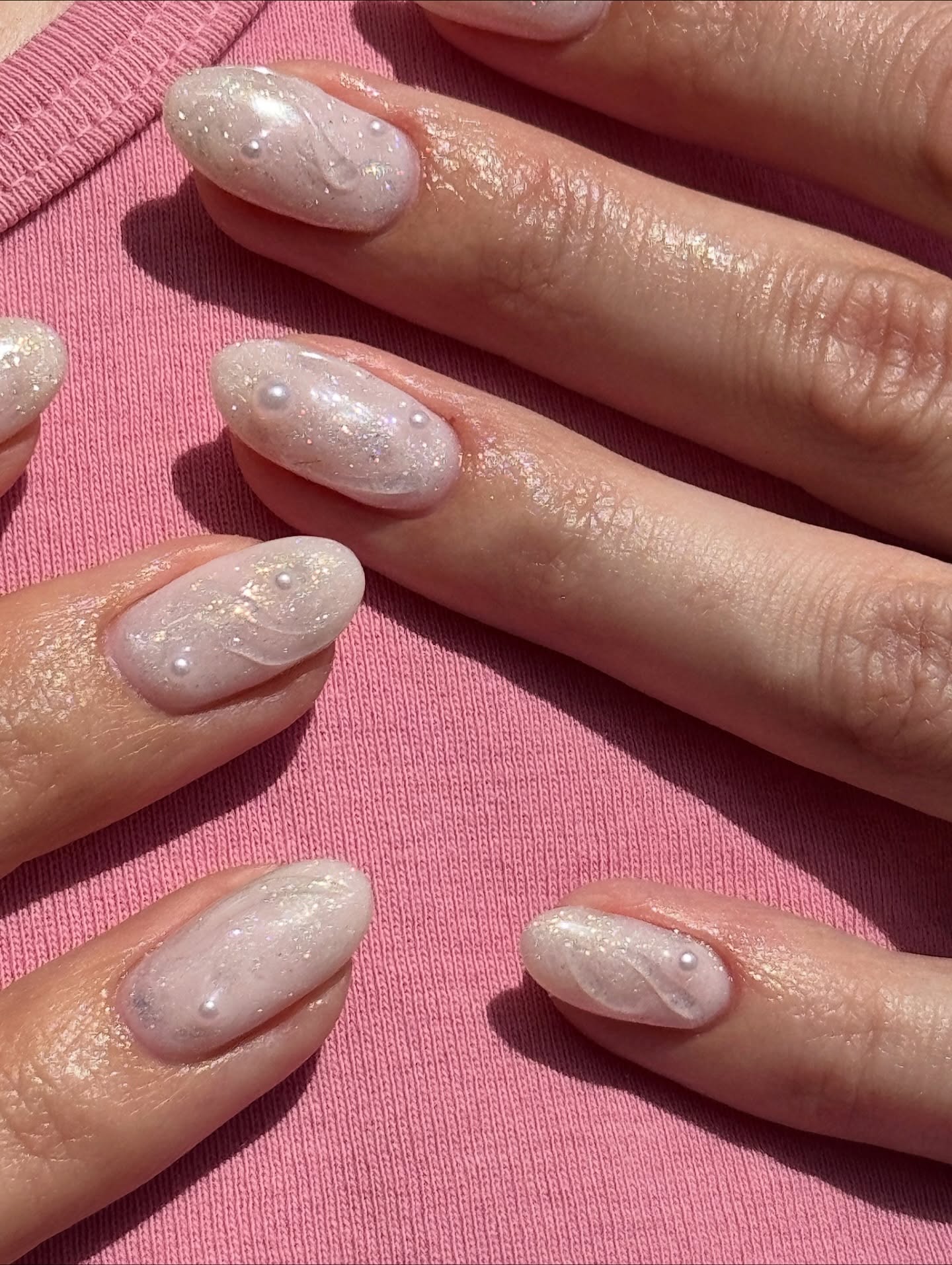 Short almond-shaped nails coated in hazy white shimmer with subtle raised swirls and tiny pearl accents