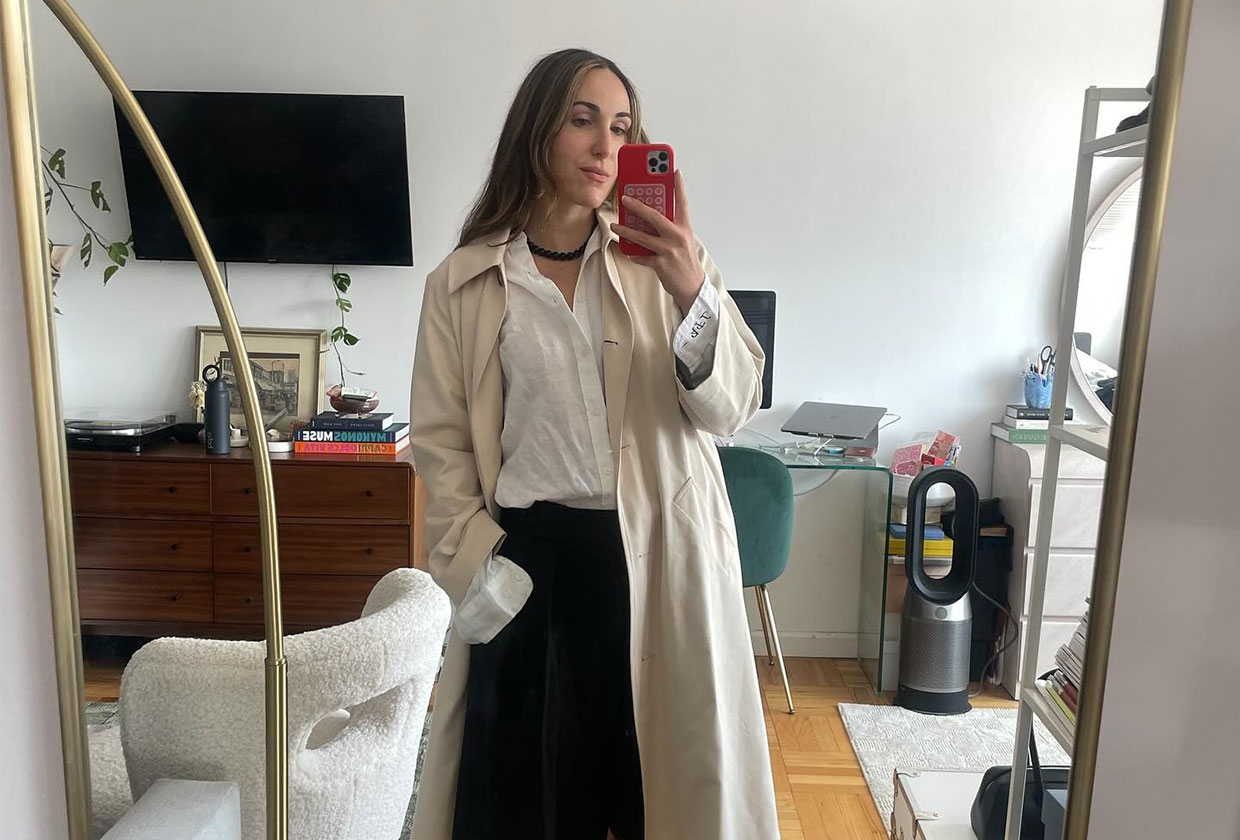 Woman wearing a tan trench coat over a button-down and black trousers.
