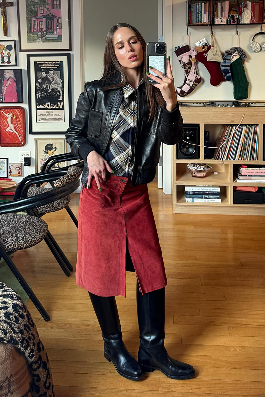 A woman wearing a leather jacket, plaid undershirt, red skirt, and black boots