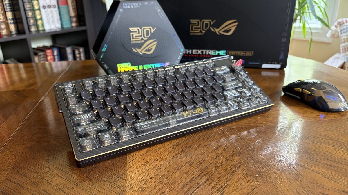 ASUS ROG mechanical keyboard and wireless mouse on a wooden table, with ROG-branded boxes in the background.