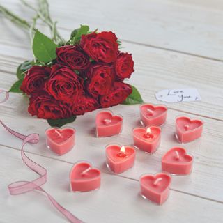 Heart shaped tealight candles on tabletop next to bouquet of roses