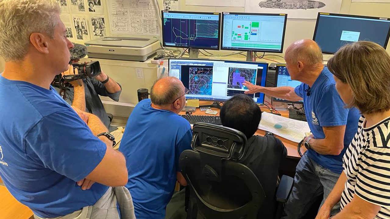 A group of five people look at computer screens charting the shipwreck's location on the seafloor.