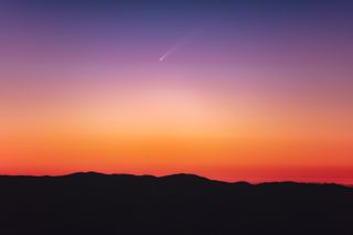 a comet soars through the sky with a long white tail. the early morning sky is awash with color, with vivid hues of orange, red and purple.