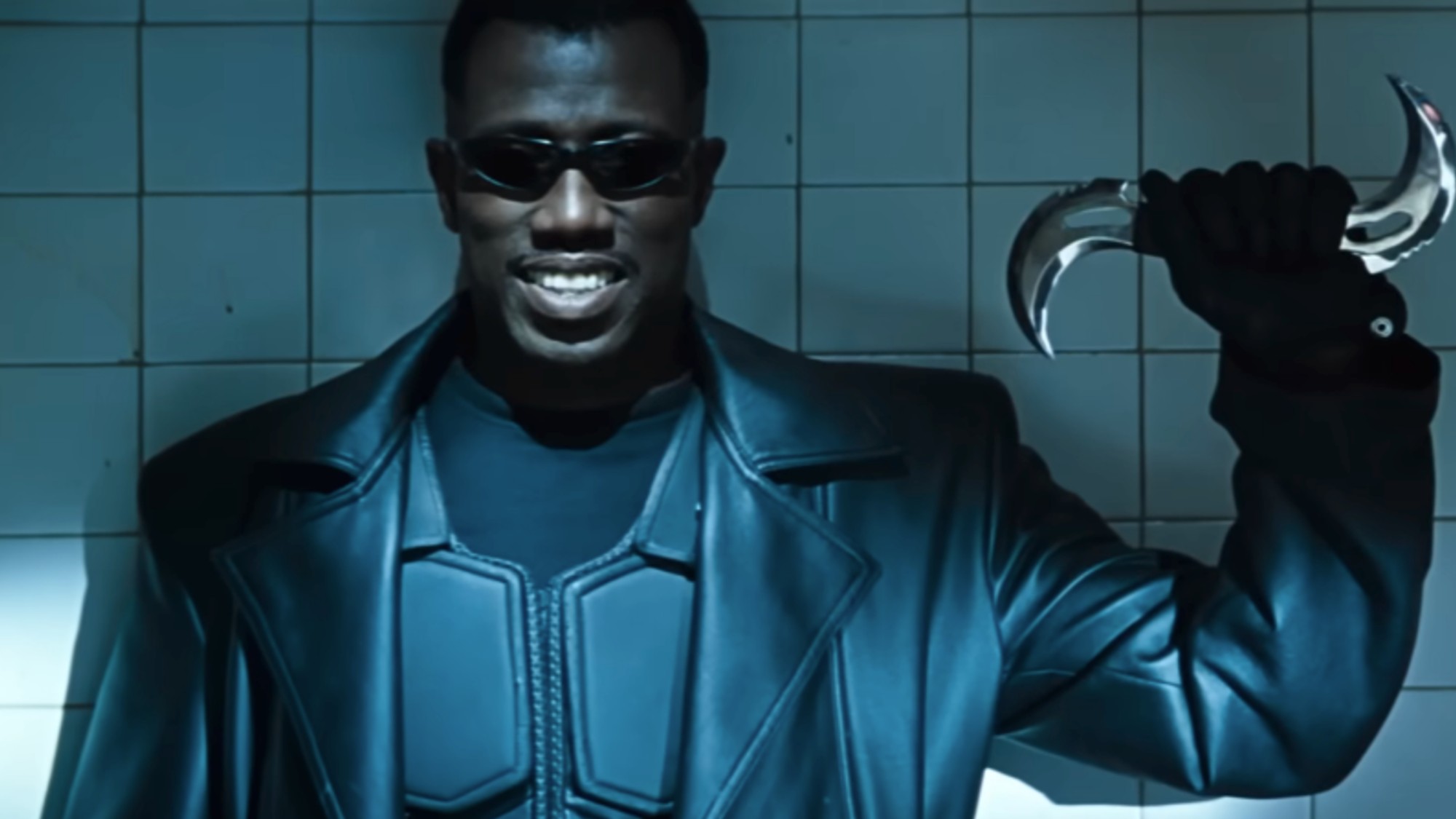 Wesley Snipes as Blade, smiling in all black and sunglasses with a silver weapon in his left hand. 