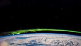 A photograph of the Aurora Borealis with green spiral tendrils taken from the International Space Station