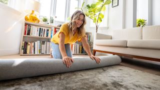 Woman rolling up rug in living room at home