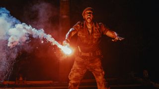 Mahershala Ali dressed in fatigues while creaming with a flare in his hand in Jurassic World Rebirth.