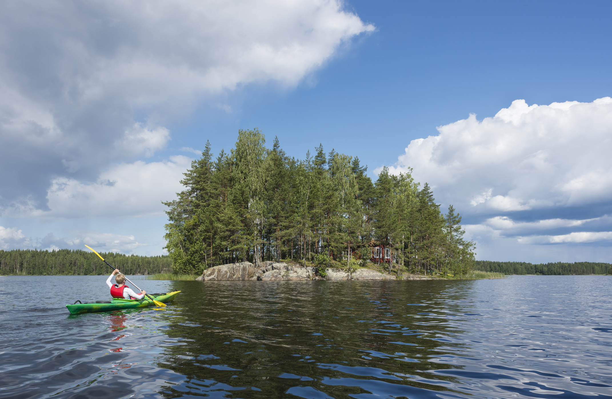 Finland, Southern Savonia, Oravi, boy kayaking on Lake Saimaa to small island with lonely hut