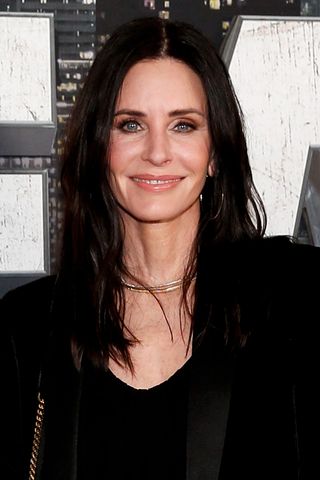 Courteney Cox on a red carpet wearing a gold choker necklace